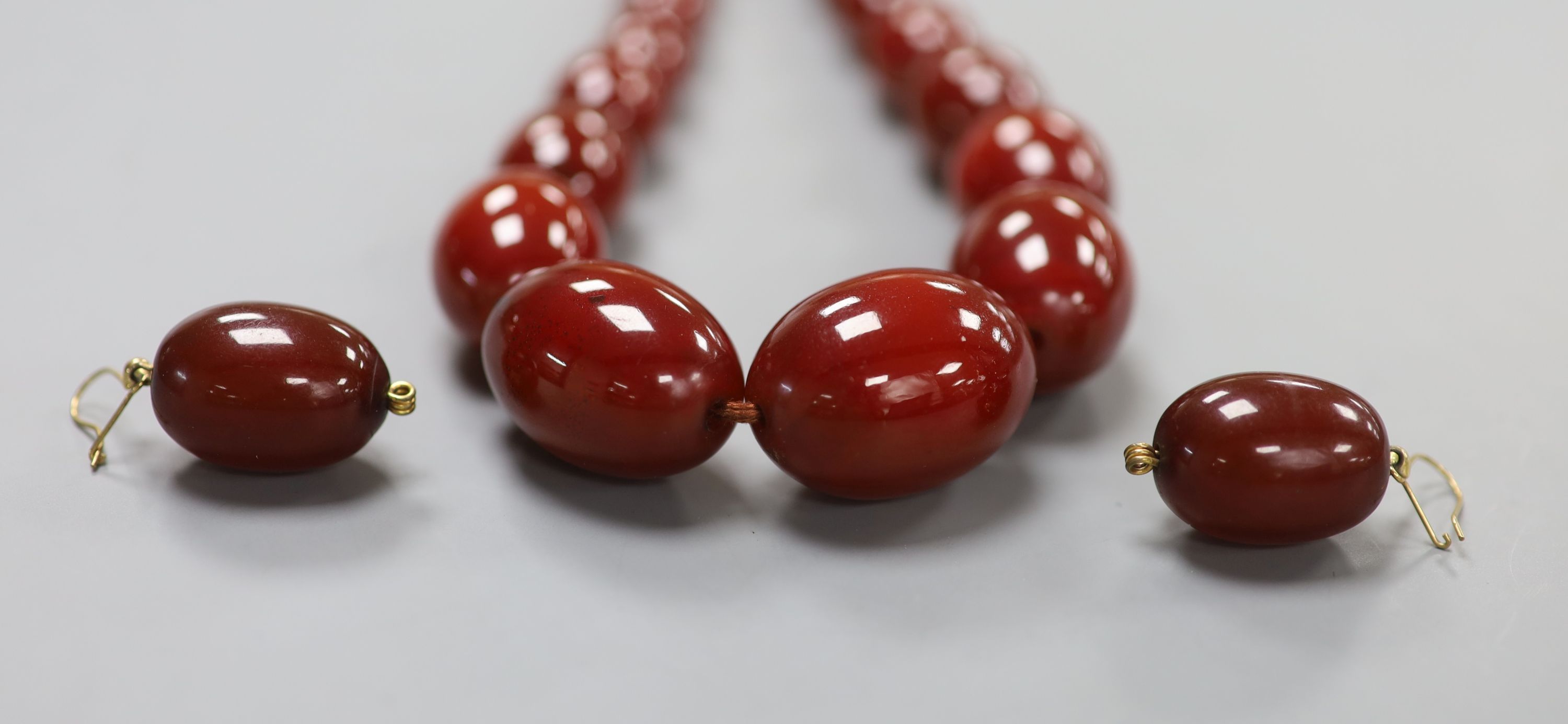 A single strand simulated oval amber bead necklace, 52cm and a pair of similar earrings, gross 94 grams.